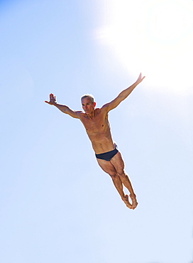 Athletic swimmer mid-air against blue sky