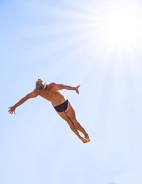 Athletic swimmer mid-air against blue sky