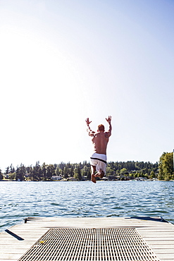 Young man jumping to lake from jetty, USA, Washington, Bellingham 