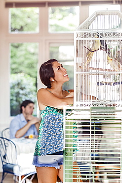 Woman standing by bird cage, man in background