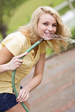 Portrait of young woman holding garden hose