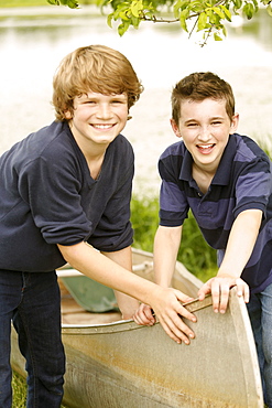 Two boys (12-13) posing with boat on grass near lake, USA, New Jersey, Old Wick 