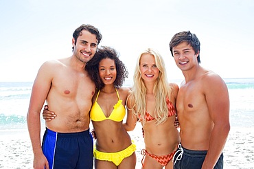 Four friends smiling as they embrace each other on a beach