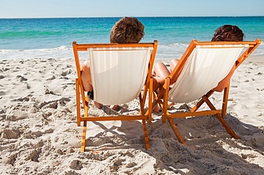 Rear view of people taking a sunbath on deck chairs