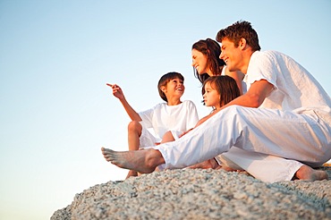 Family sitting on a natural stone wall together as the son points in front of him