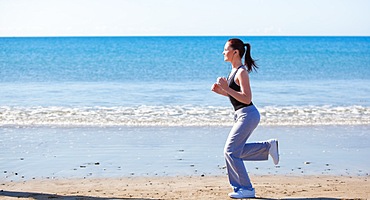 Sporty woman running on the beach and listening to music