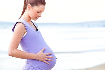 Pregnant beautiful woman watchning her stomach on the beach