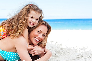 Side view of a girl lying on her mothers back on the beach