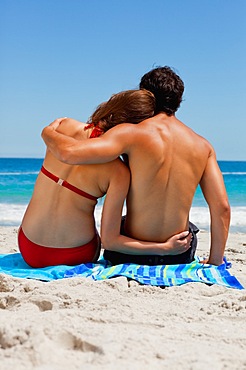 Rear view of a tanned duo in love sitting on a beach towel