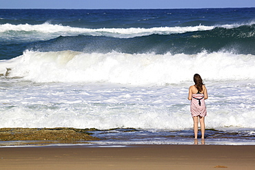 A young woman stands by crashing waves at the beach, St. Lucia Wetlands, Kwa-Zulu Natal, South Africa, Africa