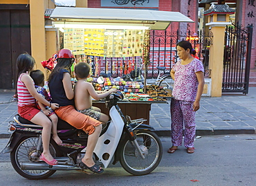 Children stop by on their motorbike to look at trinkets being sold by a woman with a push cart, Hoi An, Vietnam, Indochina, Southeast Asia, Asia