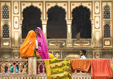 Two women in brightly ed saris gossiping at the holy 'Monkey Palace' of Galta, Jaipur, Rajasthan, India