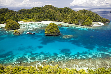 A dive liveaboard rests in a beautiful bay, roped to limestone islands.  Raja Ampat, Papua, Indonesia, Pacific Ocean.