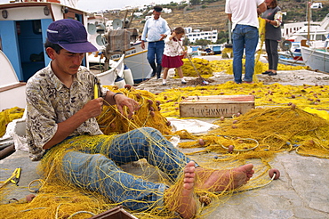 Fisherman using hands and feet to repair fishing net on Mykonos, Cyclades Islands, Greek Islands, Greece, Europe