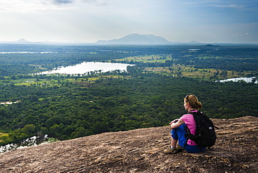 Woman sitting on Pidurangala Rock, looking at the jungle landscape of North Central Province, Sri Lanka, Asia