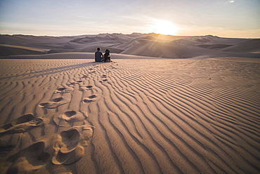 Couple watching the sunset over sand dunes in the desert at Huacachina, Ica Region, Peru, South America