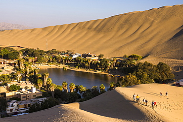 Tourists climbing sand dunes at sunset at Huacachina, a village in the desert, Ica Region, Peru, South America