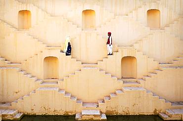 A Hindu man and woman dressed in traditional clothing, walk down the maze steps of Panna Meena ka Kund Stepwell, Amer, Rajasthan, India, Asia