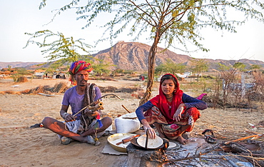 Hindu girl cooking while her father plays musical instrument in Pushkar, Rajasthan, India, Asia