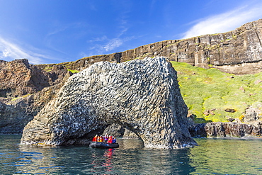 Zodiac cruises through a natural arch of columnar basalt on the southern coast of Disko Island, Kuannersuit, Greenland, Polar Regions