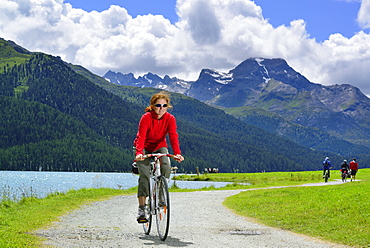 Woman cycling along Lake Silvaplana, Upper Engadin, Engadin, Canton of Graubuenden, Switzerland