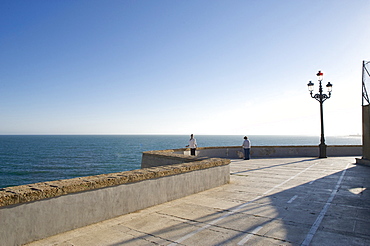 Promenade by the sea with wall and old style electric light, view across the sea with two lonesome people, Cadiz, Andalusia, Spain, Europe