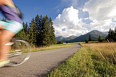 Young woman riding her bike near mountains on a sunny day, Tannheimer Tal, Tyrol, Austria