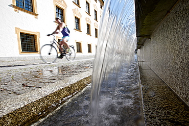 Young female cyclist riding past a fountain, Kempten, Bavaria, Germany