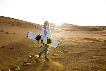 young woman with snowboard, sand dunes near Merzouga, Erg Chebbi, Sahara Desert, Morocco, Africa