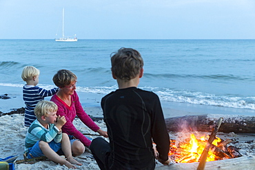 Familiy with children sitting around the campfire, adventure, sailing boat, dream beach between Strandmarken und Dueodde, sandy beach, summer, Baltic sea, Bornholm, Strandmarken, Denmark, Europe, MR