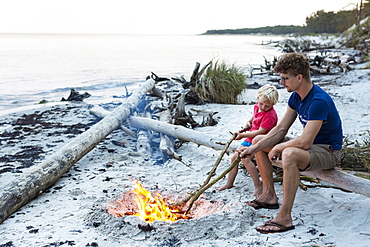 Five year old boy sitting with his father around a campfire, adventure, dream beach between Strandmarken und Dueodde, sandy beach, summer, Baltic sea, Bornholm, Strandmarken, Denmark, Europe, MR