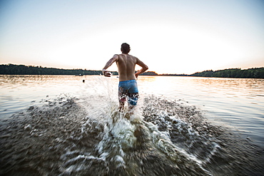 Young man running into the water of a lake, Freilassing, Bavaria, Germany