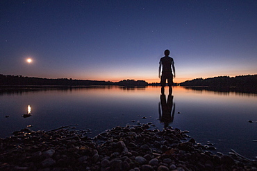 Young man standing in a lake at night, Freilassing, Bavaria, Germany