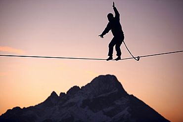 Man balancing on a slackline in sunset, Oberstdorf, Bavaria, Germany