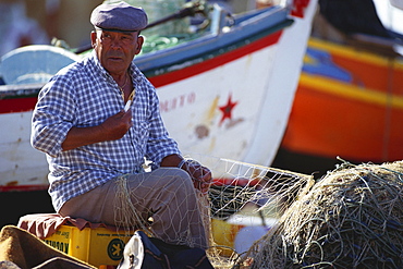 Fisherman repairing a fishing net at harbour, Algarve, Portugal, Europe