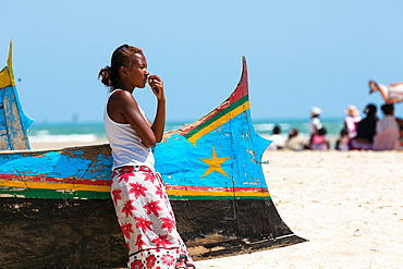 Young woman leaning on fishing boat on the beach at Morondava, Madagascar, Africa