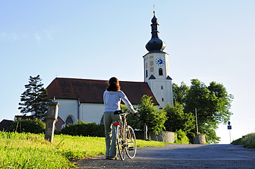 Woman pushing bicycle, Assumption of Mary pilgrimage church, Bad Koetzting, Bavarian Forest, Lower Bavaria, Bavaria, Germany