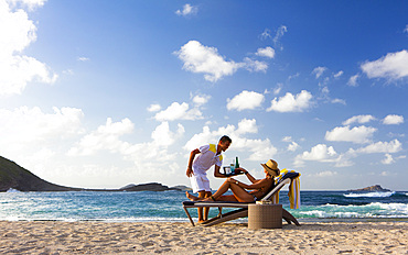 Beach service. Woman being served by waiter on the beach. St. Barths.