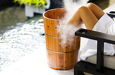 A woman having a footbath, in wooden barrel , with steam billowing. Horizontal. Kuala Lumpur, Malaysia.