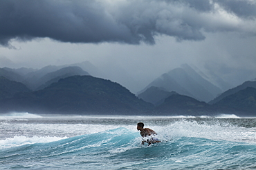 Surfer on wave in Teahupoo surfing area with storm clouds and mountains behind, Tahiti Iti, Tahiti, Windward Islands, French Polynesia, South Pacific