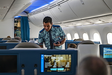 Flight attendant hands menu to passenger in Poerava Business Class aboard Air Tahiti Nui Boeing 787 Dreamliner airplane on the flight from Paris Charles de Gaulle Airport (CDG) in France to Los Angeles International Airport (LAX) in the United States