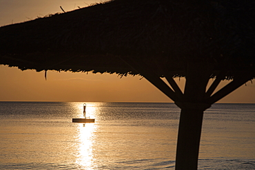 Silhouette of thatched parasol and young woman on bathing platform in the water in front of Ong Lang Beach, Ong Lang, Phu Quoc Island, Kien Giang, Vietnam, Asia