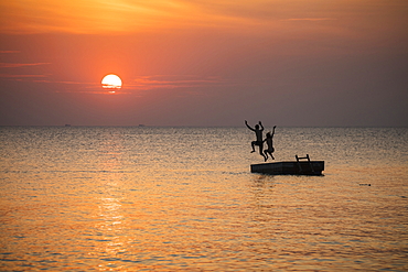 Silhouette of a young couple jumping from a bathing platform in front of Ong Lang Beach at sunset, Ong Lang, Phu Quoc Island, Kien Giang, Vietnam, Asia