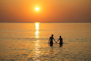 Silhouette of a romantic young couple holding hands in the water in front of Ong Lang Beach at sunset, Ong Lang, Phu Quoc Island, Kien Giang, Vietnam, Asia