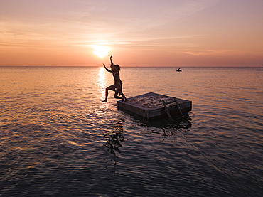 Aerial view silhouette of young couple jumping from a bathing platform at sunset on Ong Lang Beach, Ong Lang, Phu Quoc Island, Kien Giang, Vietnam, Asia