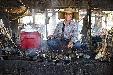 Happy woman with grilled fish at a street food stall at the market, Oudong (Udong), Kampong Speu, Cambodia, Asia