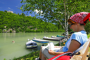 Woman sitting on bench near river Danube while reading, Neuhaus castle, Danube Cycle Route Passau to Vienna, Upper Austria, Austria