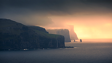 Sunset with clouds on the coast of Eysteroy with steep cliffs and rock formation Risin og Kellingin, Faroe Islands