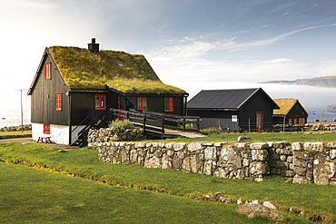 Black houses with red windows and a grass roof in the village of Kirkjubøur on Streymoy in the sun, Faroe Islands