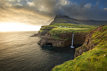 Sunset at the Múlafossur waterfall with the village of Gásadalur on the island of Vagar, Faroe Islands